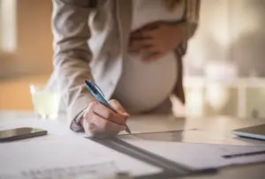 A pregnant woman signing a document.
