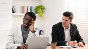 A white coworker staring with disdain at his black coworker.