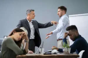 A boss yelling at an employee while two other coworkers are sitting quietly.