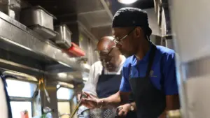 A chef cooking and his boss is thinking in the background.
