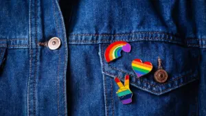 Three rainbow colored pins on a denim jacket.