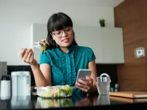 A woman eating lunch while looking at her phone.