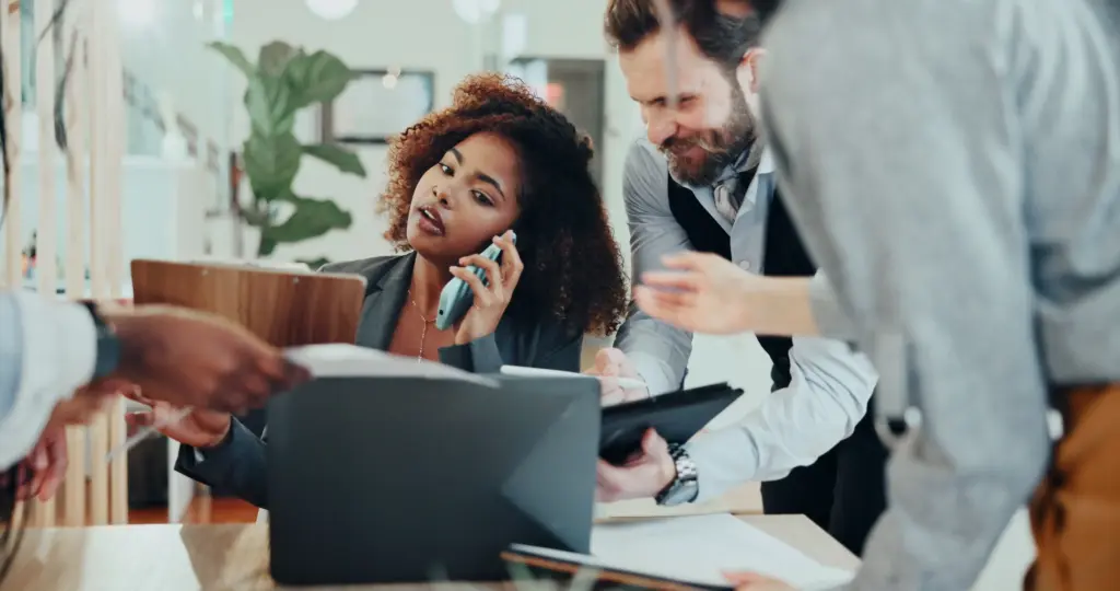 A woman on the phone at work while multiple coworkers are asking for things.