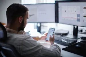 A man texting while looking at information on his computer.