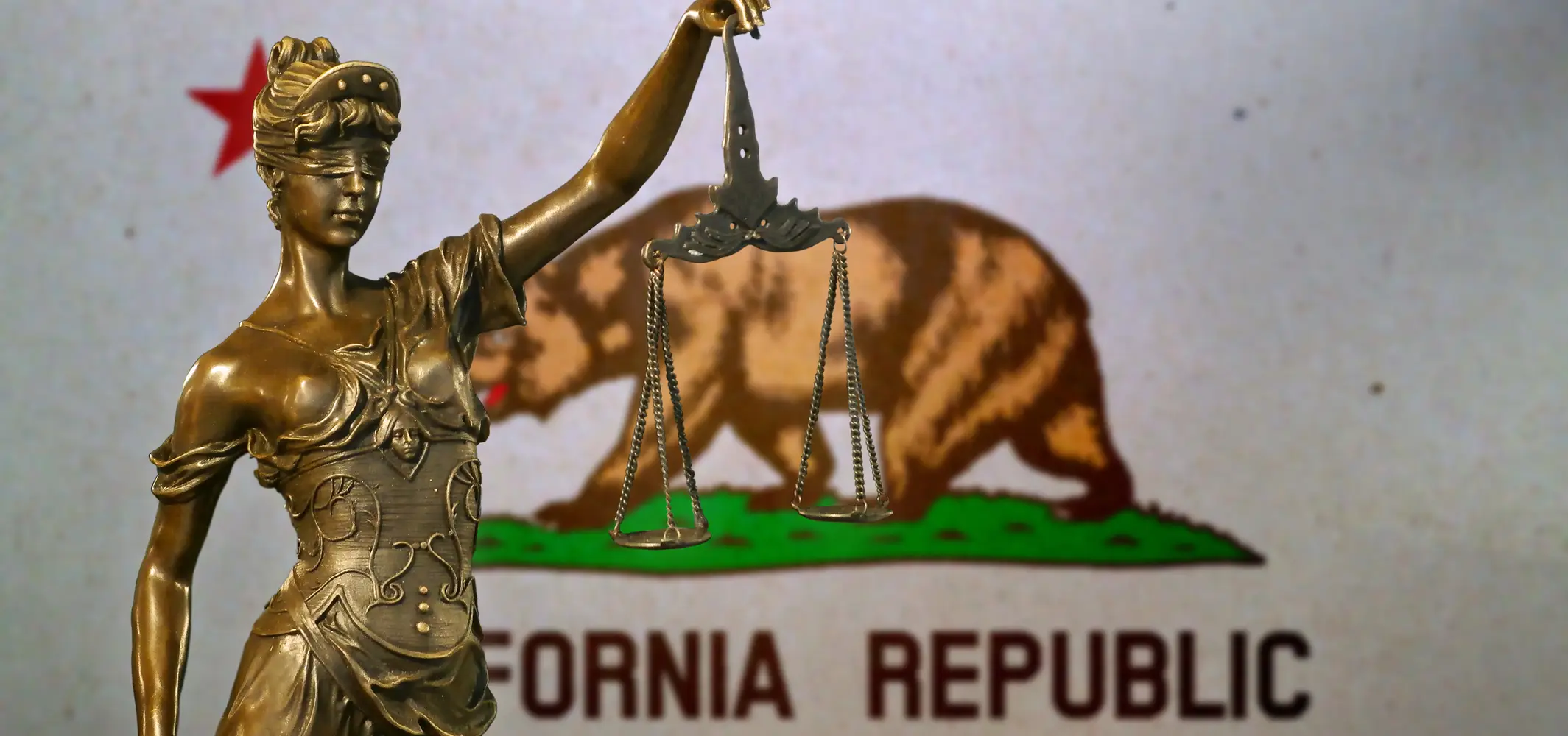A statue of Lady Justice in front of the California state flag.