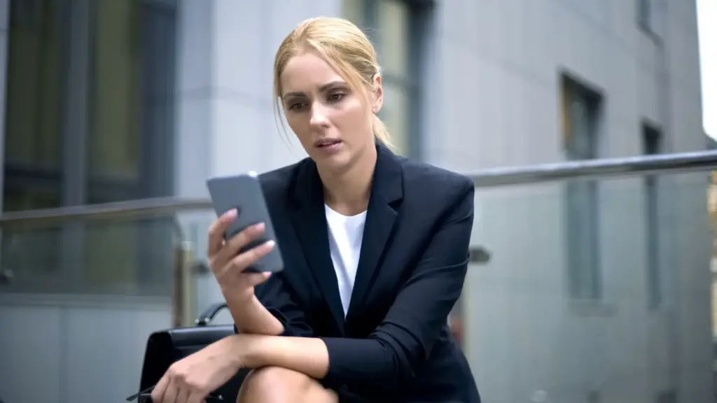 A woman looking at her phone in shock after finding out her data was hacked.