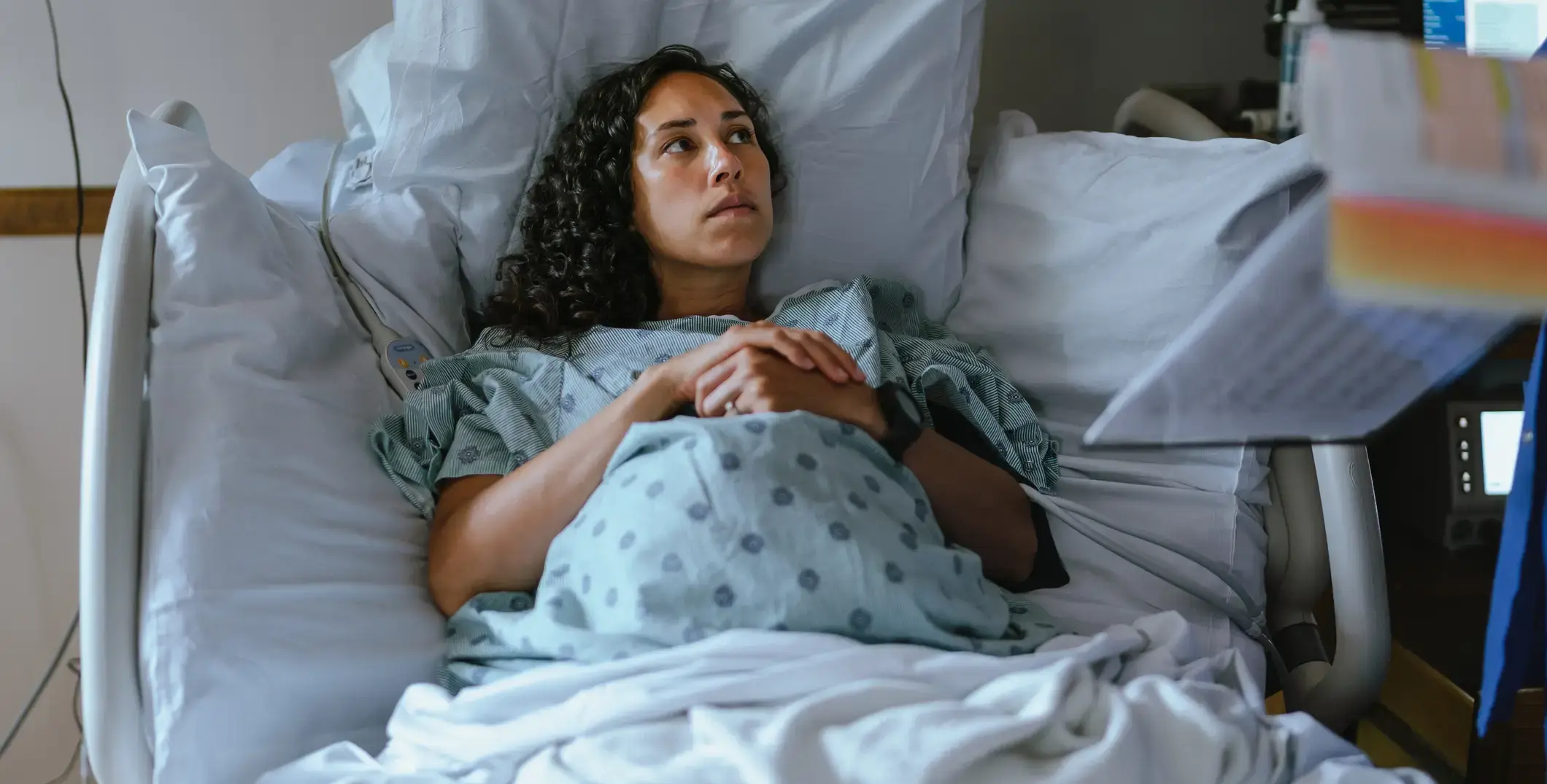 A pregnant woman sitting in a hospital bed concerned.