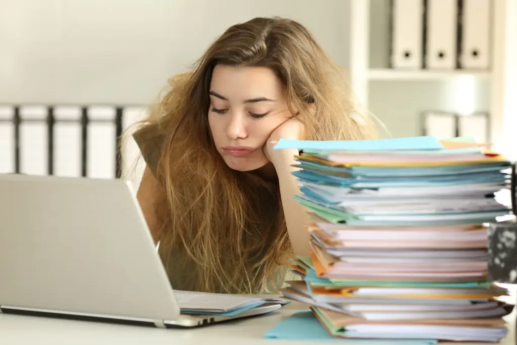 An overworked intern with a stack of folders on her desk.