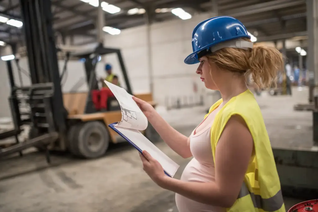 A pregnant warehouse worker looking at her clipboard. 