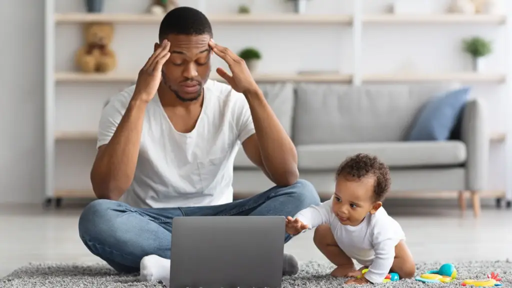 A confused father on the phone and laptop while his baby is grabbing the computer. 