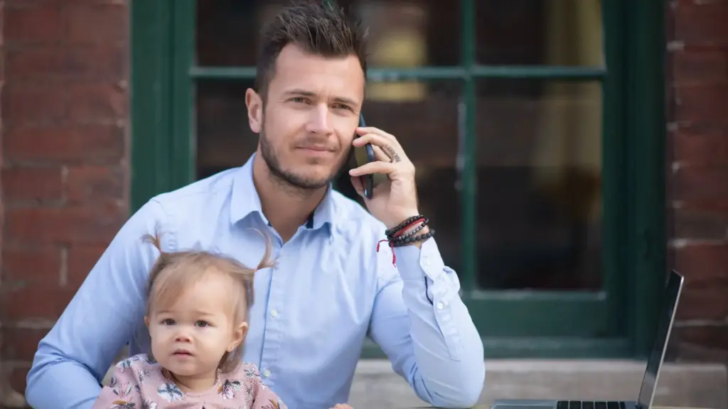 A father on the phone with his job while holding his daughter.