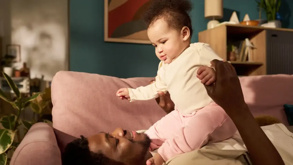 A father laying down and holding his child up in the air. 