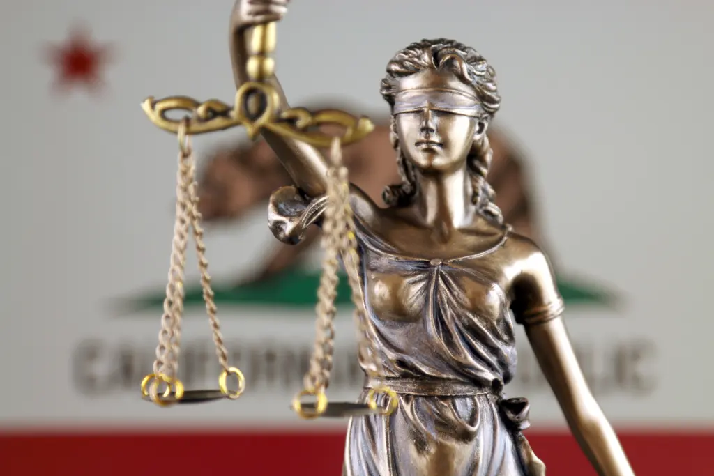 A statue of lady justice in front of the California flag.