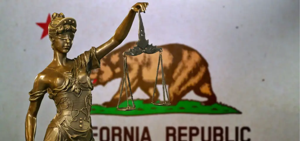 A statute of lady justice in front of the California flag.