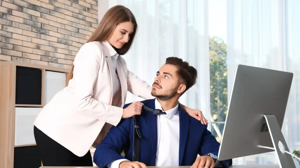 A woman approaching her coworker and grabbing his tie in a seductive manner.