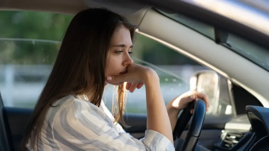A woman staring in space inside her car because of workplace retaliation.
