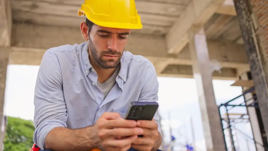 A construction worker looking at his phone with concerns about his wage.